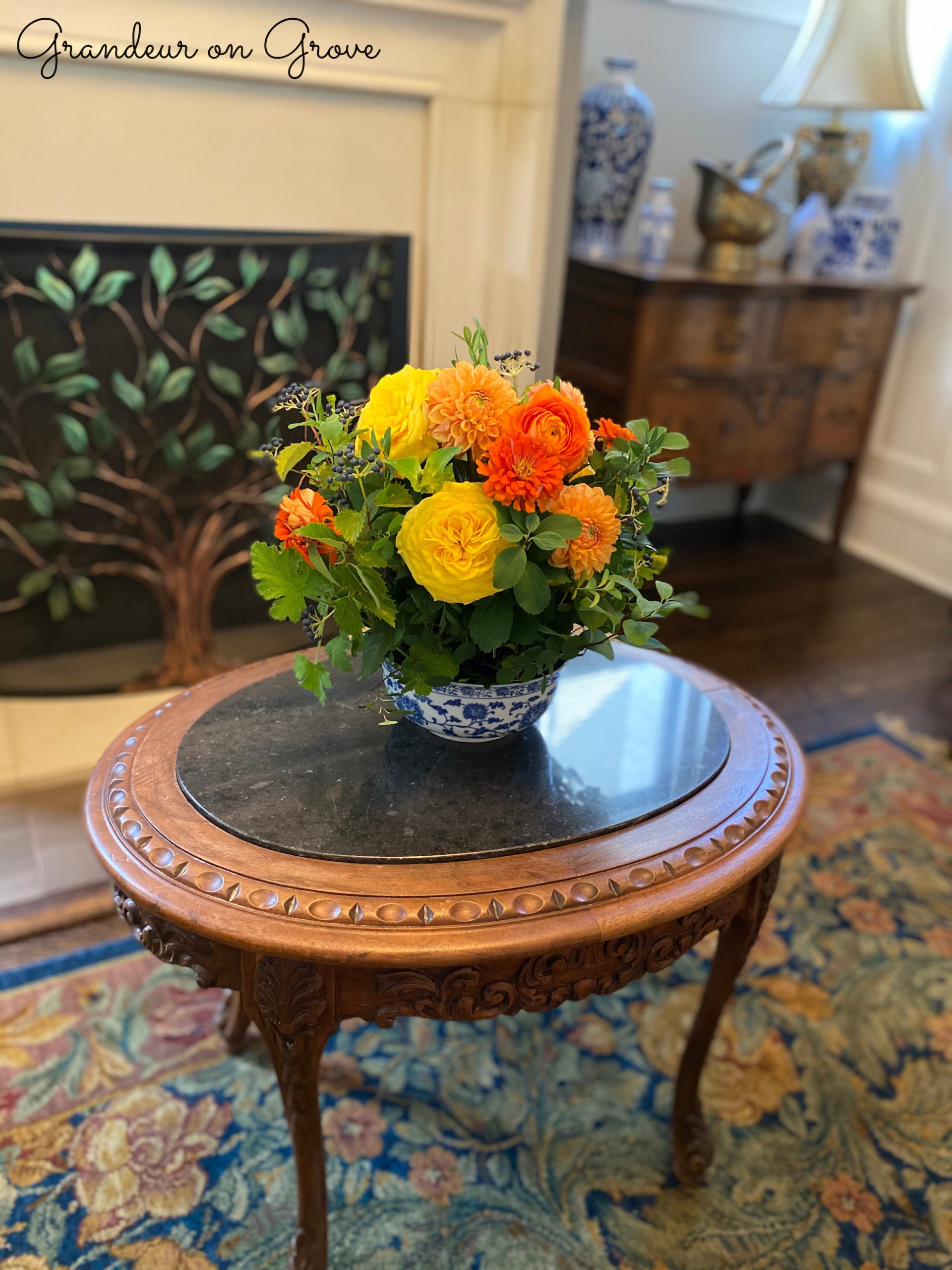 An orange and yellow floral arrangement sits on an antique coffee table