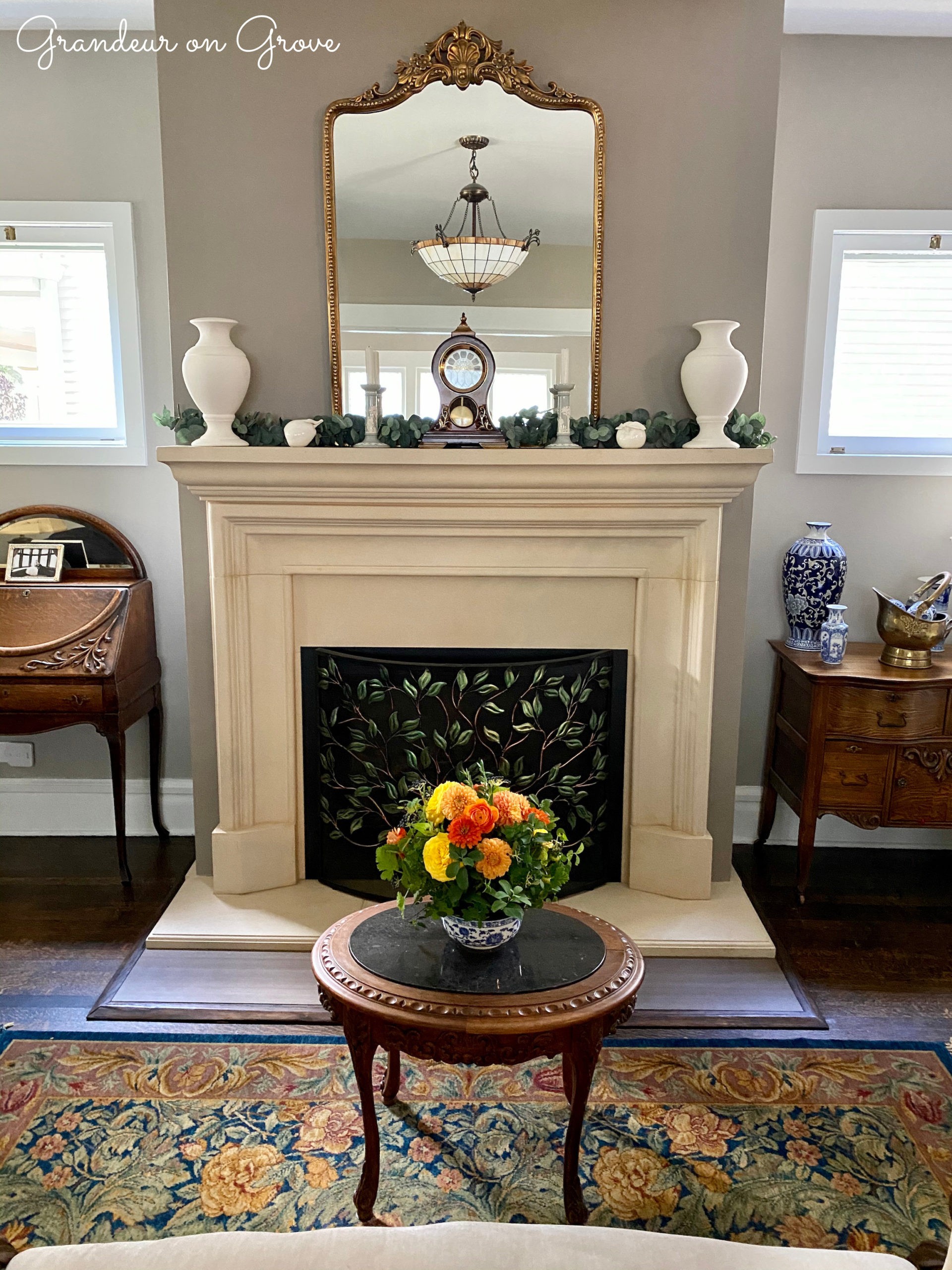 A fireplace with a bouquet of orange and yellow flowers on a table